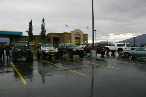 2003 Jeep TJ - Several off-road vehicles, including a silver 2003 Jeep TJ, are parked in a lot on a cloudy day.