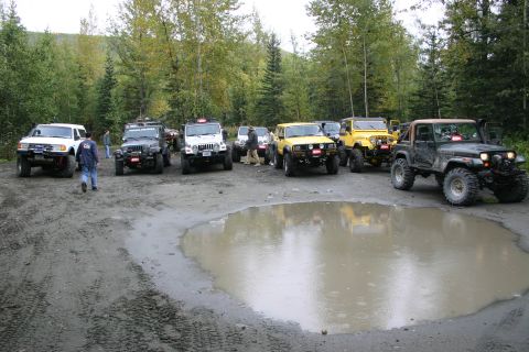 2003 Jeep TJ - Several off-road vehicles are parked in a muddy area with trees in the background.