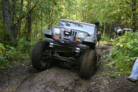 2003 Jeep TJ - A Jeep Wrangler navigates a challenging muddy off-road course with other vehicles visible in the background.