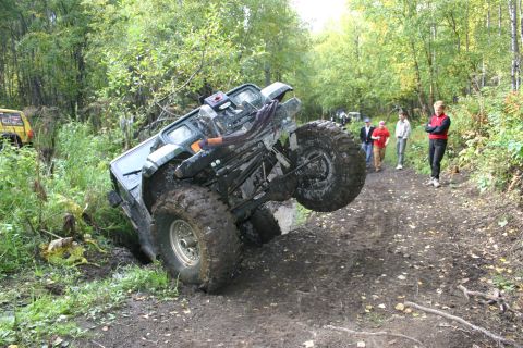 2003 Jeep TJ - An off-road vehicle is stuck in a ditch on a muddy trail, with onlookers observing the situation.