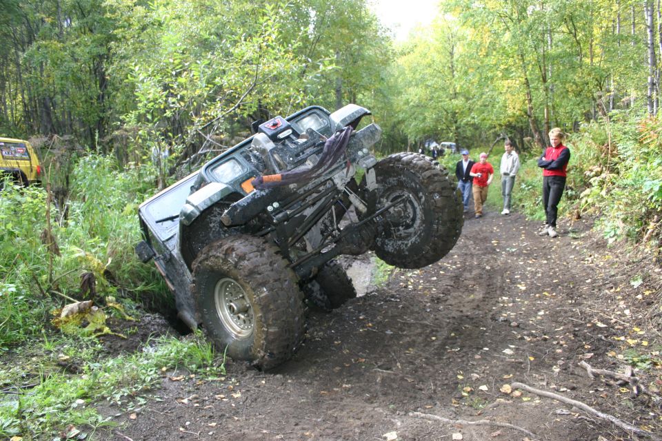 Off-road vehicle tilted in a ditch with large tires, people watching on a dirt path