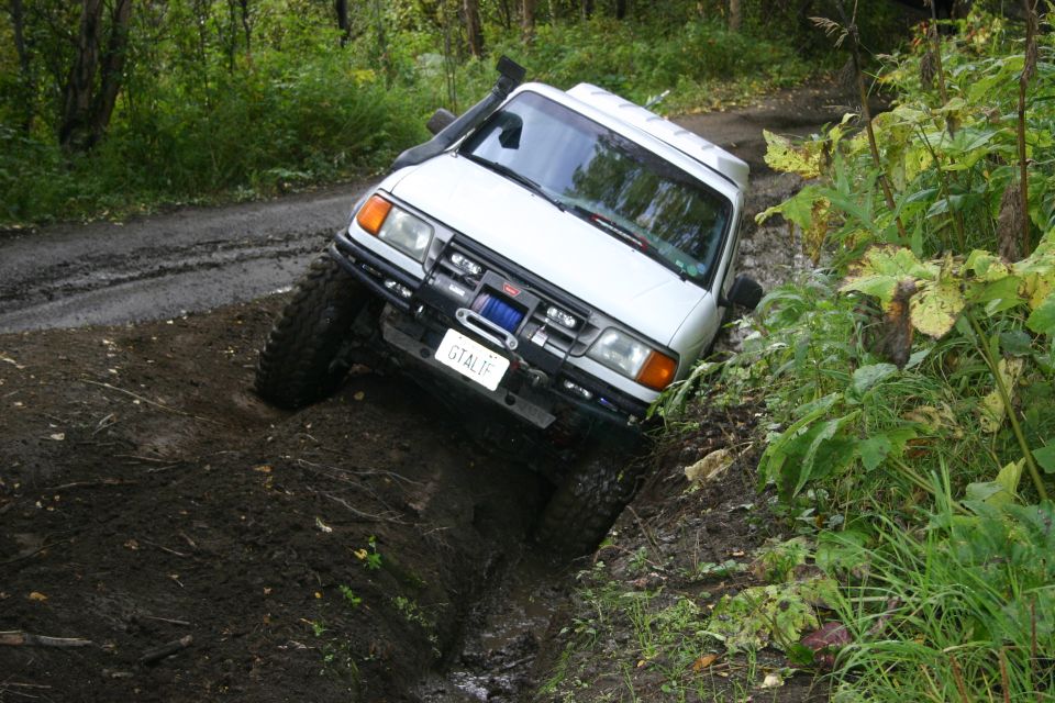 White off-road SUV with snorkel and winch navigating a muddy ditch on a dirt road