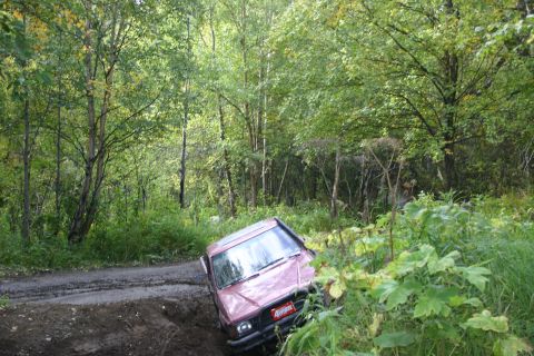 2003 Jeep TJ - A pink SUV is tilted precariously on a muddy trail surrounded by dense forest foliage.