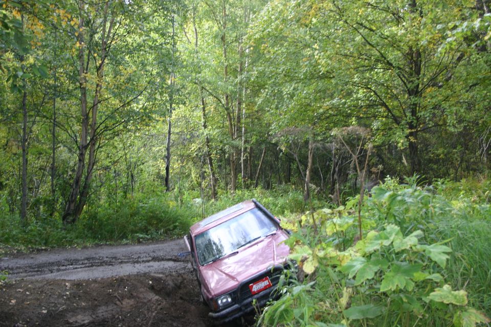 Pink SUV tilted on a muddy trail in a forest