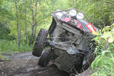2003 Jeep TJ - An off-road vehicle is stuck and tilted on its side in a muddy, wooded area.