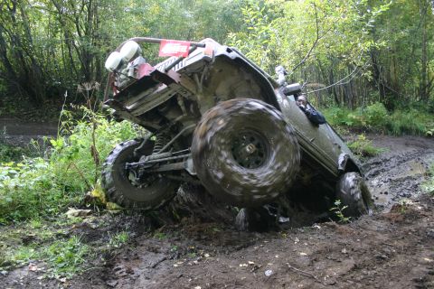 2003 Jeep TJ - An off-road vehicle is stuck in a muddy trail, with its tires spinning and body tilted precariously.