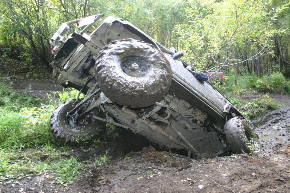 Mud-covered 2003 Jeep TJ tilted on its side in a muddy forest trail