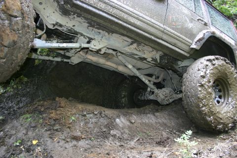 2003 Jeep TJ - Vehicle's undercarriage and suspension are visible as it is stuck in a deep mud pit.