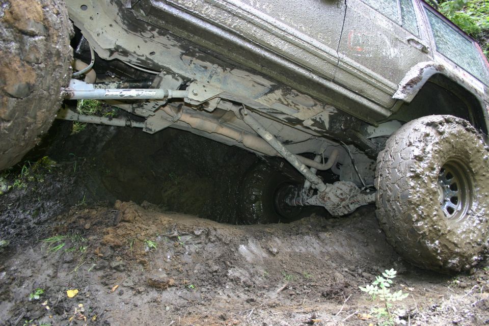 Off-road vehicle with large tires stuck in a muddy ditch, showing undercarriage and suspension components