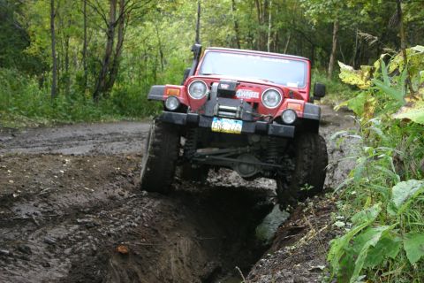 2003 Jeep TJ - This red 2003 Jeep TJ tackles a challenging muddy obstacle on an off-road trail.