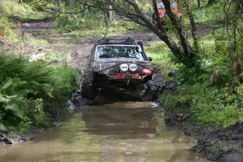 2003 Jeep TJ - A modified Jeep Cherokee XJ navigates a muddy trail, with another vehicle partially visible behind it.