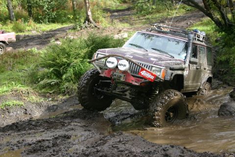 2003 Jeep TJ - A modified Jeep Cherokee XJ tackles a challenging muddy obstacle on an off-road trail.