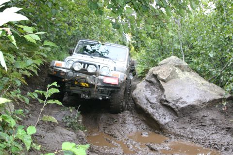 2003 Jeep TJ - A Jeep TJ tackles a challenging muddy off-road course, maneuvering around a large boulder.