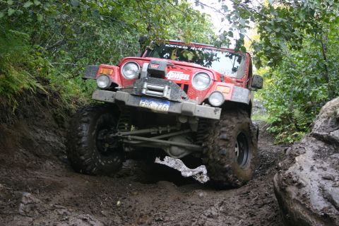 2003 Jeep TJ - This red Jeep TJ navigates a challenging muddy off-road course, its capabilities.