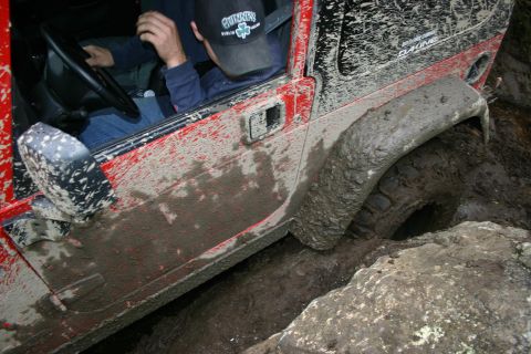 2003 Jeep TJ - A red Jeep Wrangler navigates a muddy, rocky obstacle during an off-road excursion.