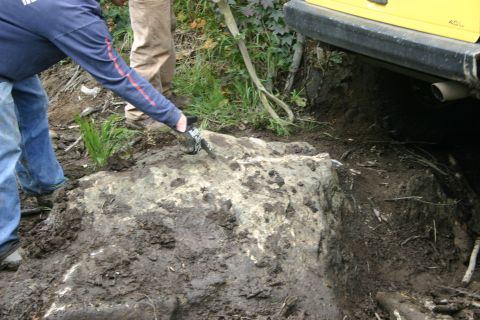 2003 Jeep TJ - A yellow vehicle's rear is partially visible as people interact with a large rock in muddy terrain.