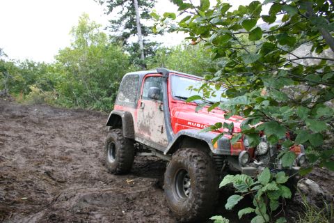2003 Jeep TJ - A red 2003 Jeep TJ Rubicon navigates a challenging muddy off-road path.