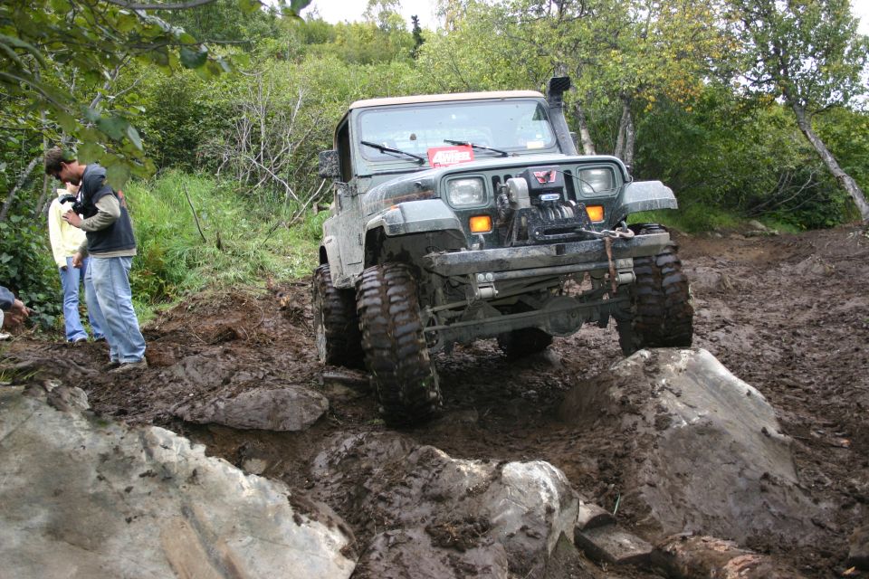 Jeep Wrangler on muddy trail, climbing over rocks. Snorkel and winch visible