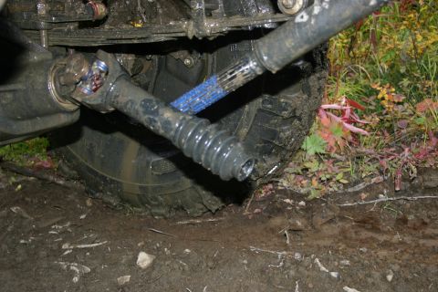 2003 Jeep TJ - Close-up view of the driveshaft and suspension components of an off-road vehicle, partially submerged in mud.