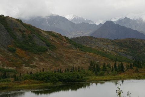 2003 Jeep TJ - A vast mountain landscape unfolds under a cloudy sky, with a calm lake reflecting the scene.