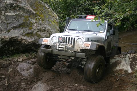 2003 Jeep TJ - A Jeep Wrangler navigates a challenging, rocky, and muddy off-road course.