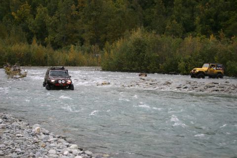 2003 Jeep TJ - Two Jeep TJs navigate a rocky riverbed surrounded by trees.