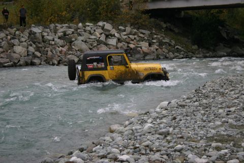 2003 Jeep TJ - A yellow 2003 Jeep TJ navigates a rocky riverbed, with "RUBICON OFF-ROAD" visible on its side.