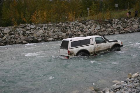 2003 Jeep TJ - A white Ford pickup truck navigates a rocky riverbed, with a snorkel attached to the intake.
