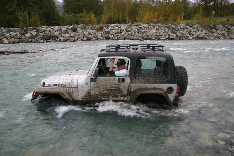 2003 Jeep TJ - A white Jeep Rubicon navigates a rocky riverbed, kicking up water as it drives through the current.