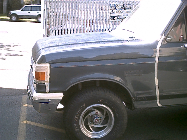 Front quarter of a dark blue Ford Bronco in a parking lot by a fence