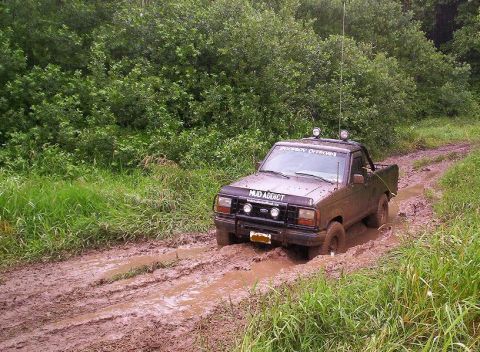 1992 Ford Ranger - A 1992 Ford Ranger navigates a challenging muddy path surrounded by lush green vegetation.