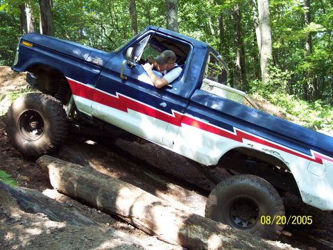 1977 Ford F-150 - This Ford pickup truck is navigating a challenging off-road course with large logs on the trail.