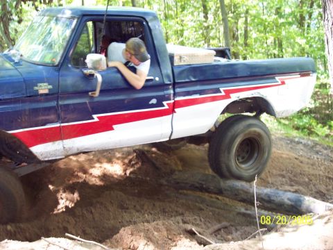 1977 Ford F-150 - A blue 1977 Ford F-150 navigates a challenging off-road course with one wheel lifted.