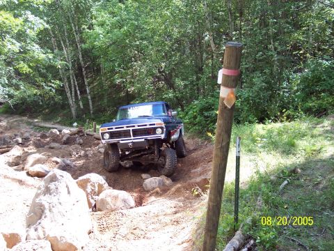1977 Ford F-150 - This truck is navigating a challenging off-road course with large rocks and trees surrounding the path.