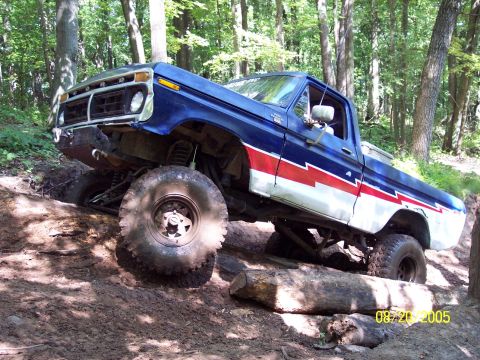 1977 Ford F-150 - A blue and white 1977 Ford F-150 navigates a challenging off-road course with large tires and lifted suspension.