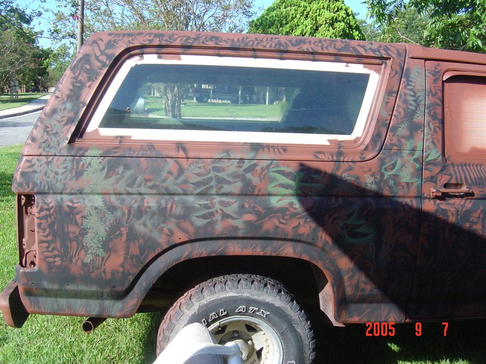 Side view of a Ford Bronco with camouflage paint. The rear quarter panel and part of the door are visible
