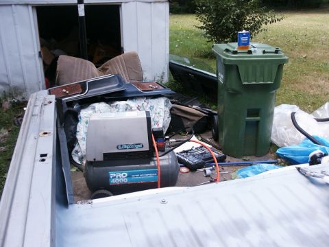 1982 Ford Bronco - Parts and an air compressor are stored in the bed of a pickup truck.