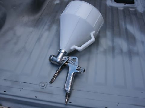 1982 Ford Bronco - Spray gun and hopper ready for undercoating application inside a vehicle.