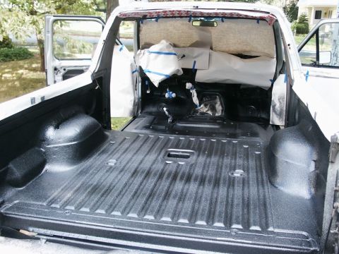 1982 Ford Bronco - The interior of a truck is taped off and has a new black spray-in liner in the bed.