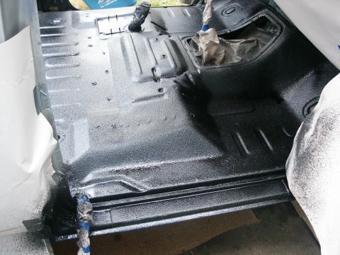 1982 Ford Bronco - The interior floor of a vehicle is being coated with a black spray-in bedliner, highlighting the textured finish and structural details.