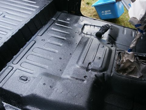 1982 Ford Bronco - Applying spray-in liner to the interior floor of a vehicle. A blue trash bin is visible in the background.