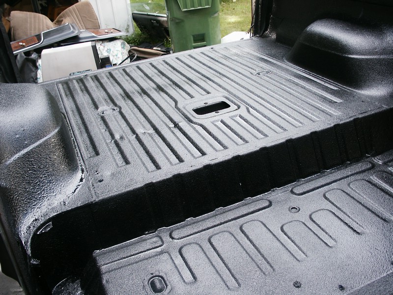 Truck bed with fresh black spray-in liner. Some seats and parts are stacked in the background