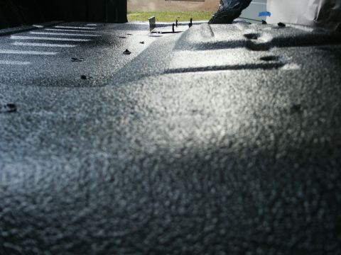 1982 Ford Bronco - The interior of a truck bed shows a dark, textured spray-in liner with visible tie-down points.
