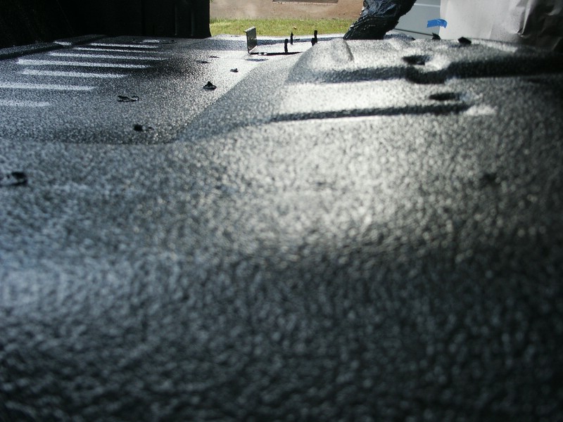 Truck bed with dark spray-in liner, showing textured surface and tie-down points