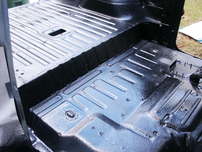 Black spray-in liner on vehicle floor with ribbed metal panels