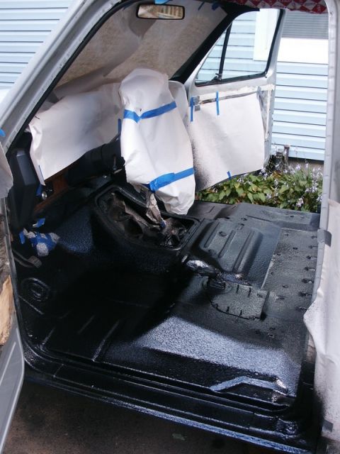 1982 Ford Bronco - The interior of a vehicle is being prepared for a spray-in liner, with seats covered and the floor coated in black.