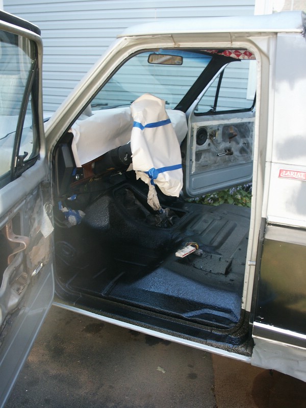 Pickup truck interior with doors open, showing floor and dashboard covered in plastic