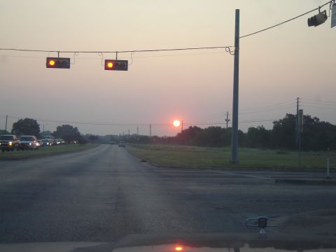 1988 Ford LTD Crown Victoria - The sun rises over a highway with a line of cars waiting at a traffic light.