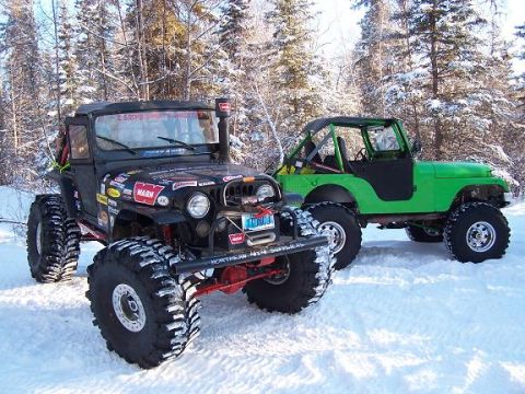 2003 Jeep TJ - Two modified Jeep Wranglers are parked in a snowy forest, one black and one green.