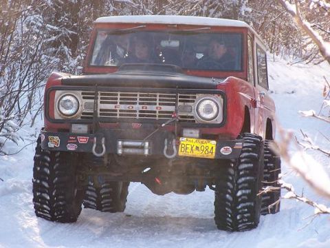 2003 Jeep TJ - A red Ford Bronco navigates a snowy trail with its occupants visible through the windshield.